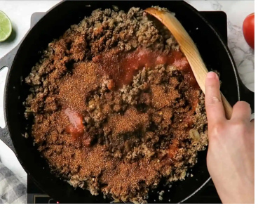 Photo of taco seasoning and water being added to the browned beef in the skillet.